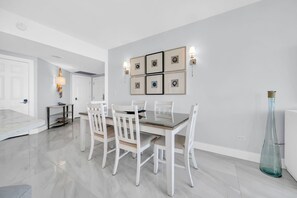 A modern dining room with a marble floor, white dining table, and chairs, a hallway with a door, and a wall with framed artwork. - St Croix's Finest ☀️Remodeled 3BR Beachfront⛱️HGTV Worthy🐟Silver Shells😎Amenities🌴 (Destin)