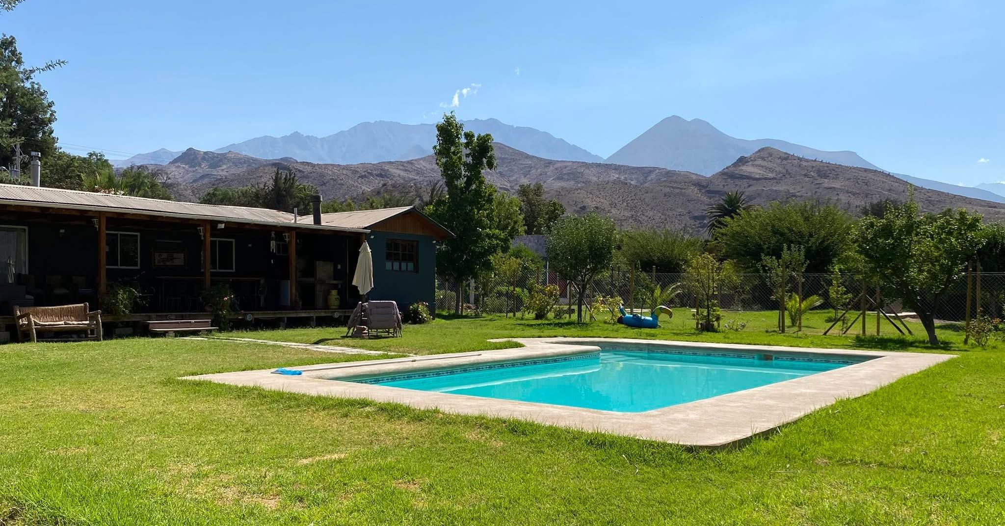 A pool with a mountain backdrop, a wooden building, and a grassy lawn.