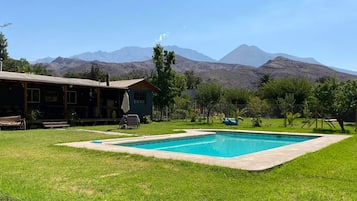 A pool with a mountain backdrop, a wooden building, and a grassy lawn.