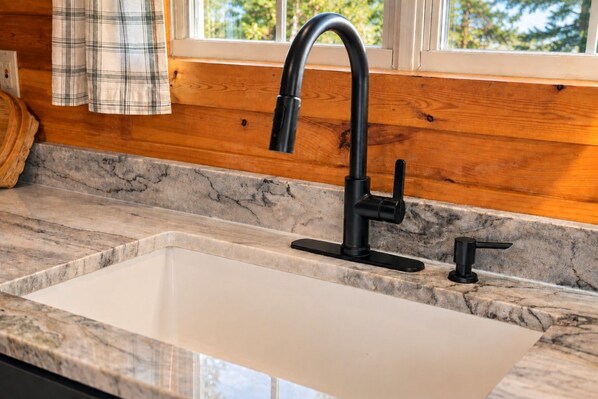 A kitchen with a black faucet, a marble countertop, and wooden paneling. - Lakefront Livin | Private Dock • Mtn Views • Game Room (Sevierville)
