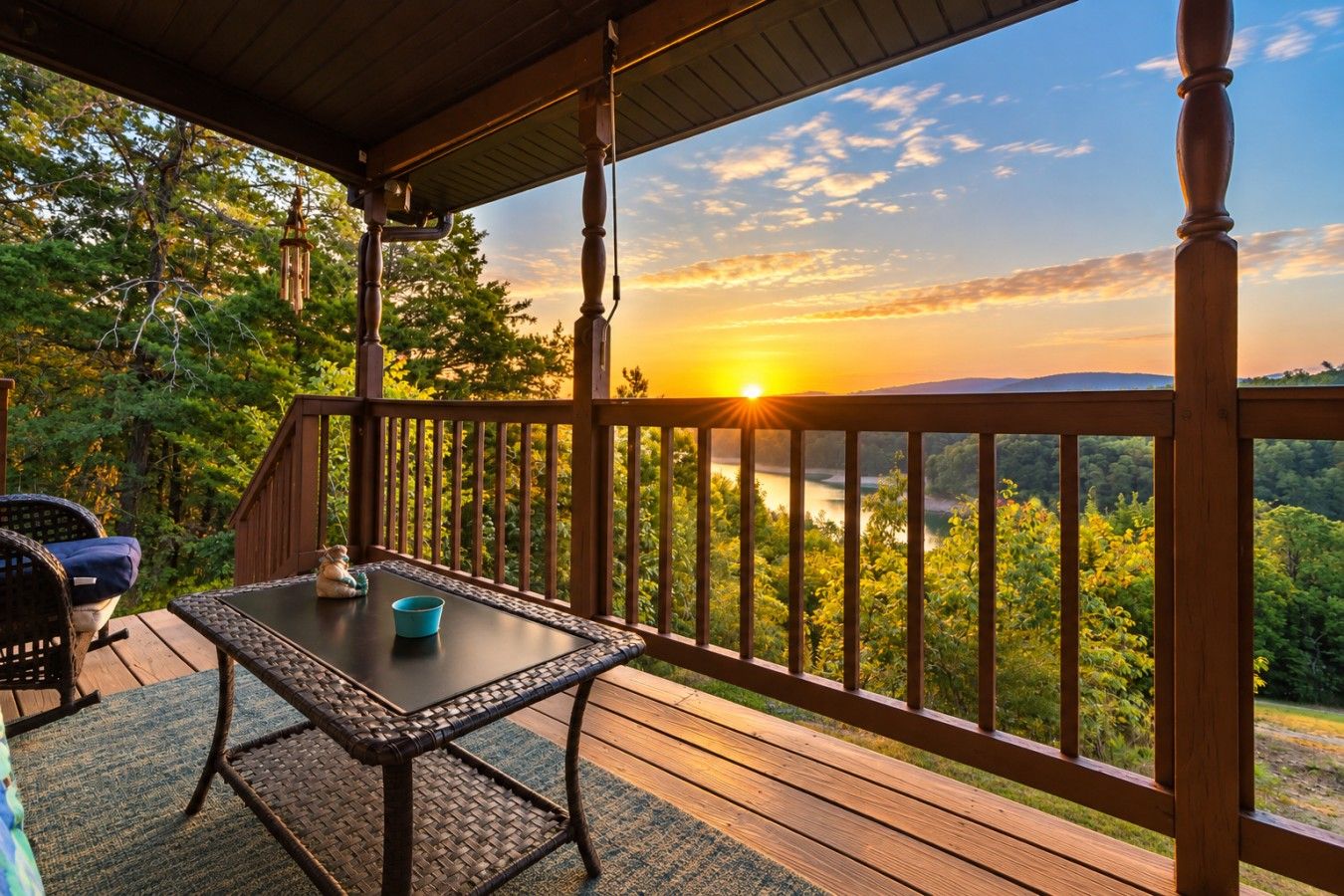 Eine Holzterrasse mit Tisch und Stühlen, mit Blick auf eine bewaldete Landschaft bei Sonnenuntergang.