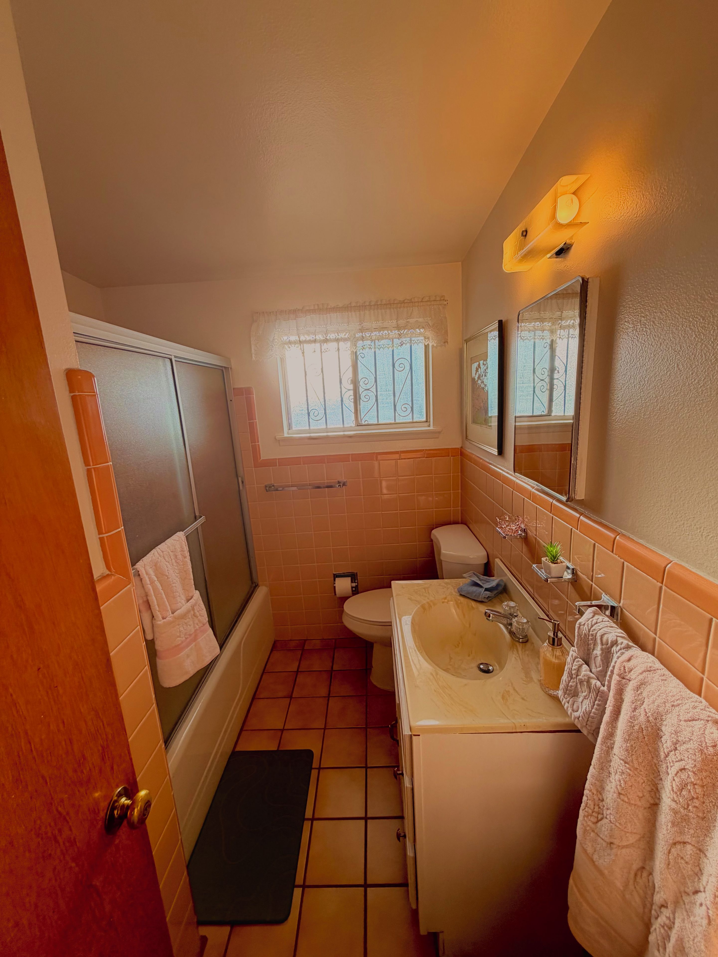 Une salle de bain équipée d’une baignoire, de toilettes, d’un lavabo et d’une fenêtre agrémentée d’un rideau décoratif.