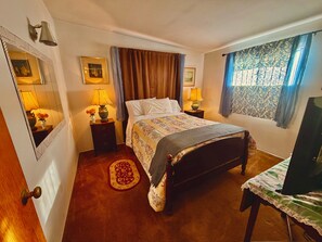 A bedroom with a bed, two bedside tables, a mirror, a window with curtains, and a television.