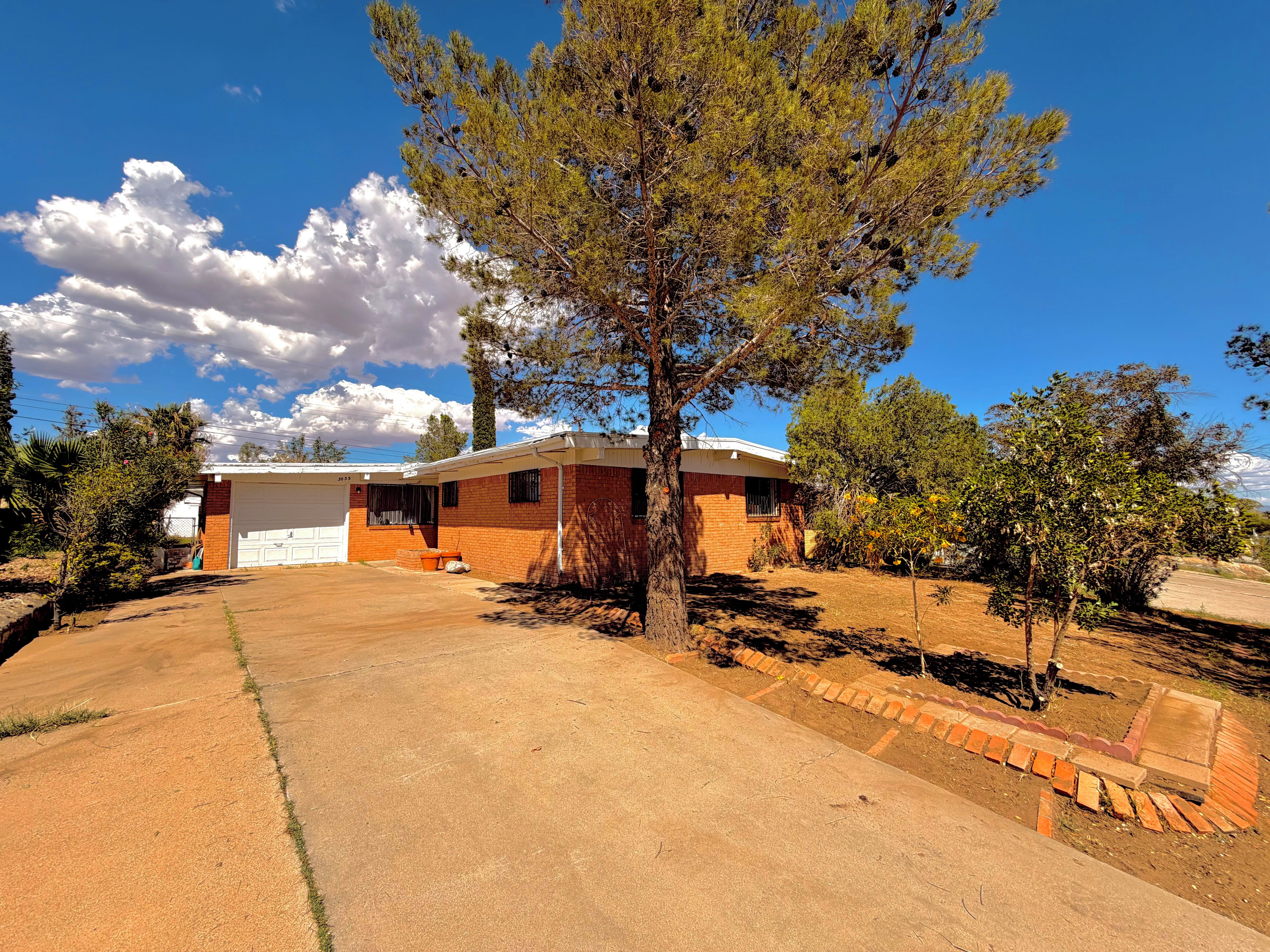 A residential property with a garage, a brick house, and a large tree in the yard.