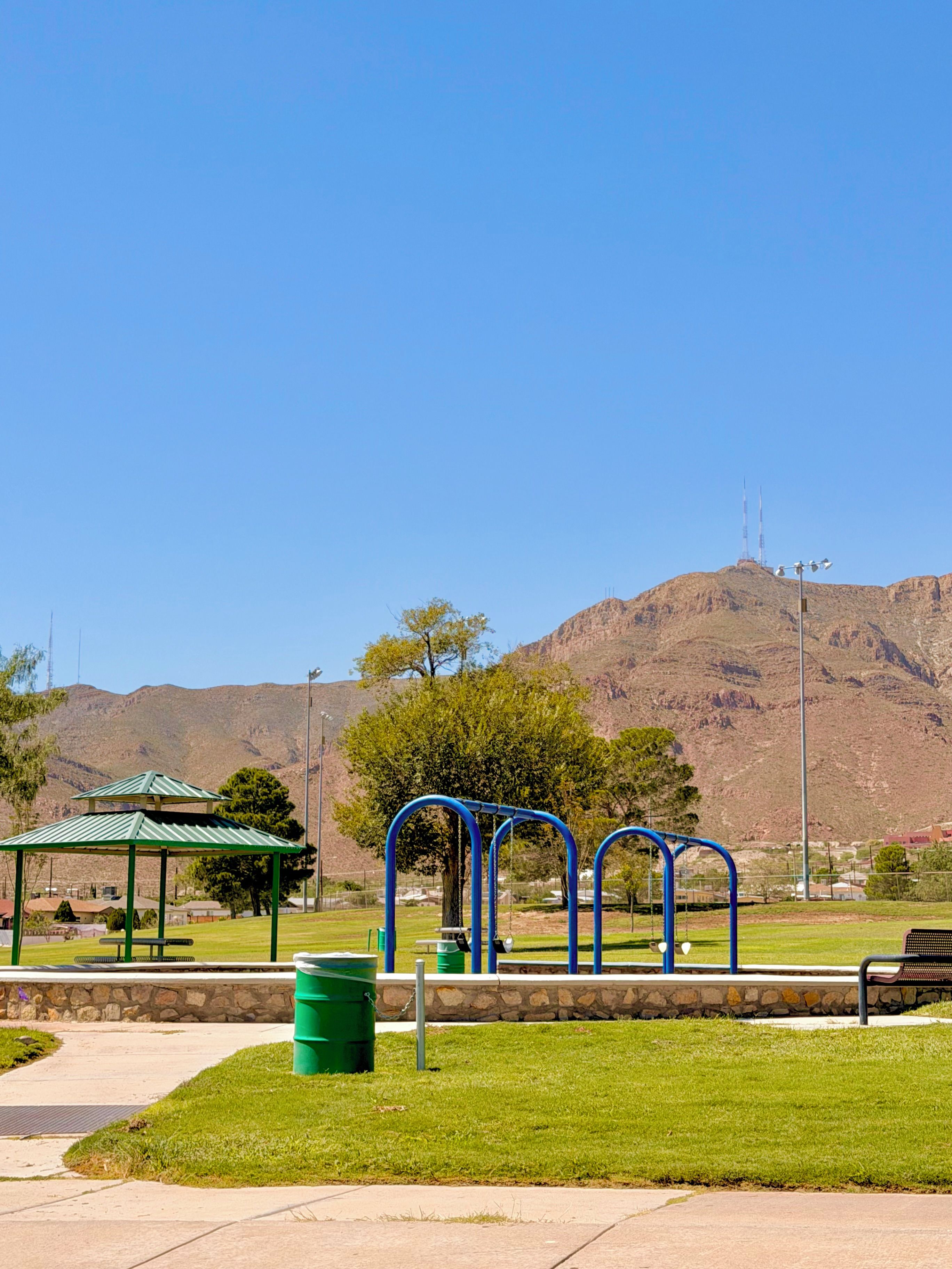 A park with exercise equipment, a gazebo, and a mountain in the background.