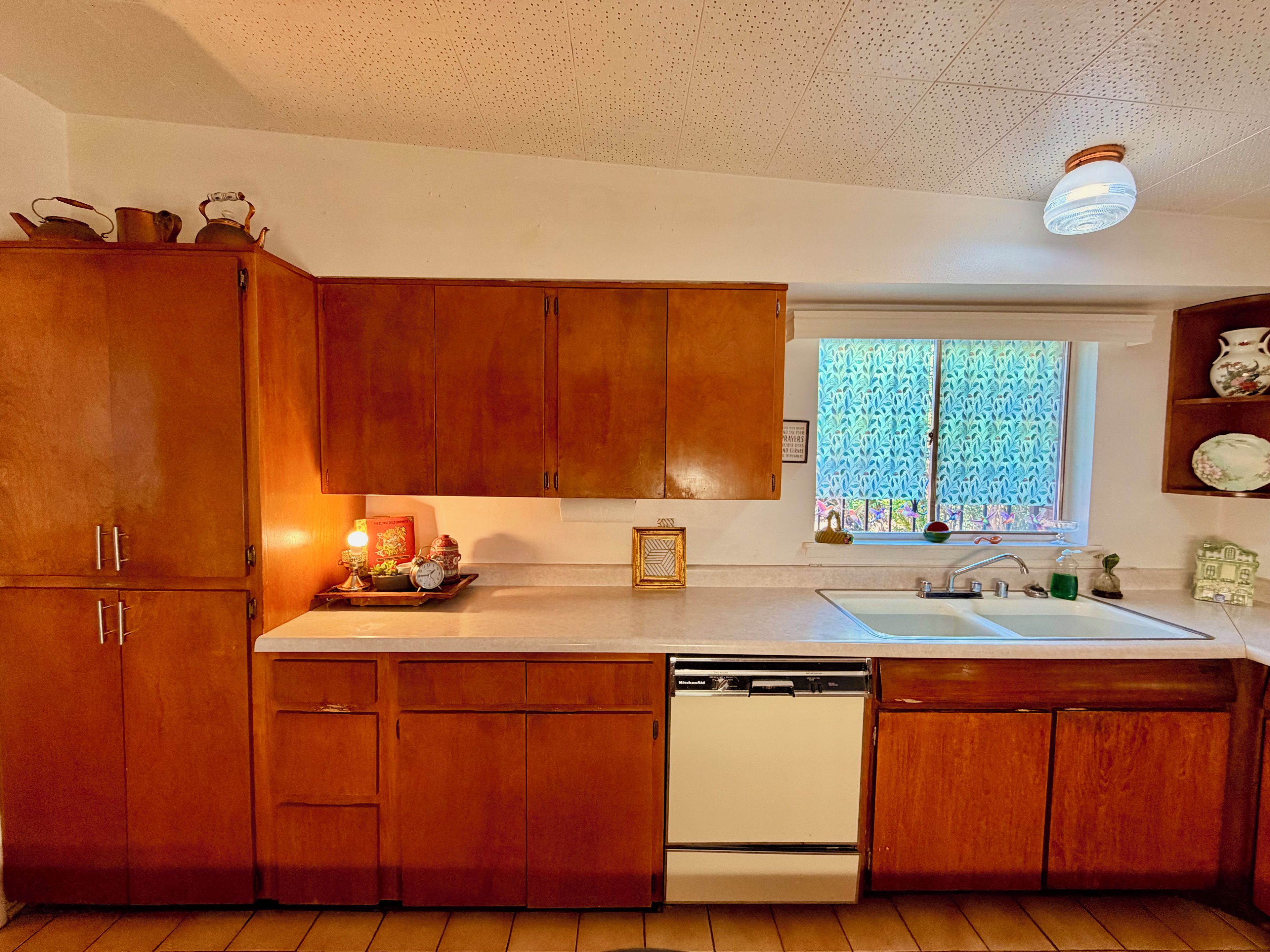 A kitchen with wooden cabinets, a dishwasher, a window with a view, and a light fixture.