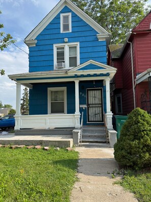 A two-story house with a front porch, a small front yard, and a mailbox.