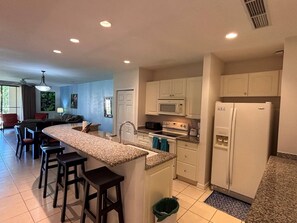 A modern kitchen with a central island, bar stools, a refrigerator, and a microwave. - The Resort Life- Pools, Beach Club, Gym, King Bed (Playas Del Coco)