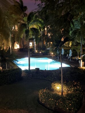 Una piscina rodeada de palmeras y sillas de descanso, con un edificio al fondo.