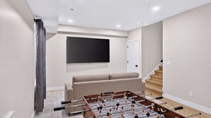 Una sala de estar moderna con mesa de fútbol, televisor de pantalla plana montado en la pared y una escalera que sube a otro nivel.