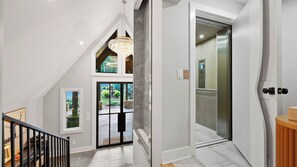 A modern interior with a staircase, a glass elevator, and a view of a garden. - Take it to the Bank by Avantstay Lakefront + Pool + Spa Dock + Kayaks Elevator Access (Denver)