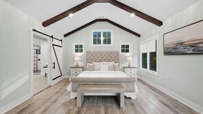 A bedroom with a vaulted ceiling, a large bed with a headboard, two bedside tables with lamps, and a bench. - Take it to the Bank by Avantstay Lakefront + Pool + Spa Dock + Kayaks Elevator Access (Denver)
