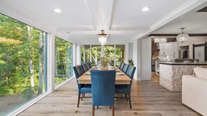Un espace de restauration moderne avec une longue table, des chaises bleues et une vue sur une forêt, visible à travers de grandes fenêtres.