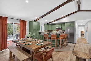 A modern kitchen with green cabinets, a stainless steel refrigerator, and a dining area with a wooden table set for four. - Stoneline Chalet - Hot Tub, Sauna, Fire Pit, Game Rm (Jewett)
