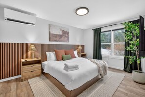 A modern bedroom with a bed, bedside tables, a lamp, a window with curtains, and a plant. - Stoneline Chalet - Hot Tub, Sauna, Fire Pit, Game Rm (Jewett)