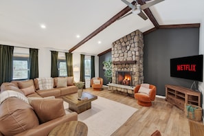 A modern living room with a stone fireplace, leather sofas, a wooden coffee table, and a flat-screen TV displaying the Netflix logo. - Stoneline Chalet - Hot Tub, Sauna, Fire Pit, Game Rm (Jewett)