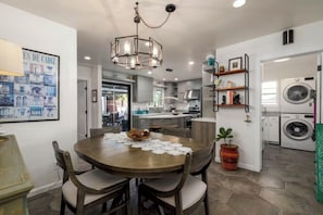 A modern kitchen with a dining area, featuring a chandelier, a large painting, and a potted plant. - Sunlit Oasis: Walk to Bay & Beach - Hot Tub, Fire Pit, BBQ & Wraparound Deck (San Diego)