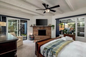 A bedroom with a bed, a TV mounted above a fireplace, and a ceiling fan. - Sunlit Oasis: Walk to Bay & Beach - Hot Tub, Fire Pit, BBQ & Wraparound Deck (San Diego)
