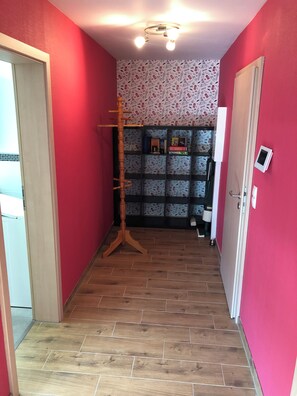Un couloir aux murs rouges, doté d’un plancher en bois et d’un luminaire au plafond.