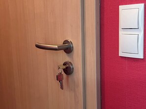 Une porte en bois avec un trou de serrure et une clé, ainsi qu’un interrupteur fixé au mur.