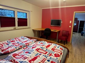 Une chambre avec deux lits, un bureau avec une chaise, une télévision et un mur rouge.