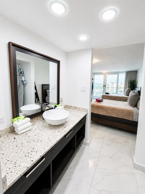 A modern bathroom with two sinks, a large mirror, and a vanity with a speckled countertop. - Elegant Beach Escape with Ocean Views Isla Verde (Carolina)
