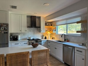 Una cocina moderna con armarios blancos, una estufa, un fregadero y un comedor con sillas de mimbre.