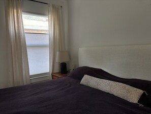 Een slaapkamer met een bed, nachtkastje, lamp en raam met gordijnen.
