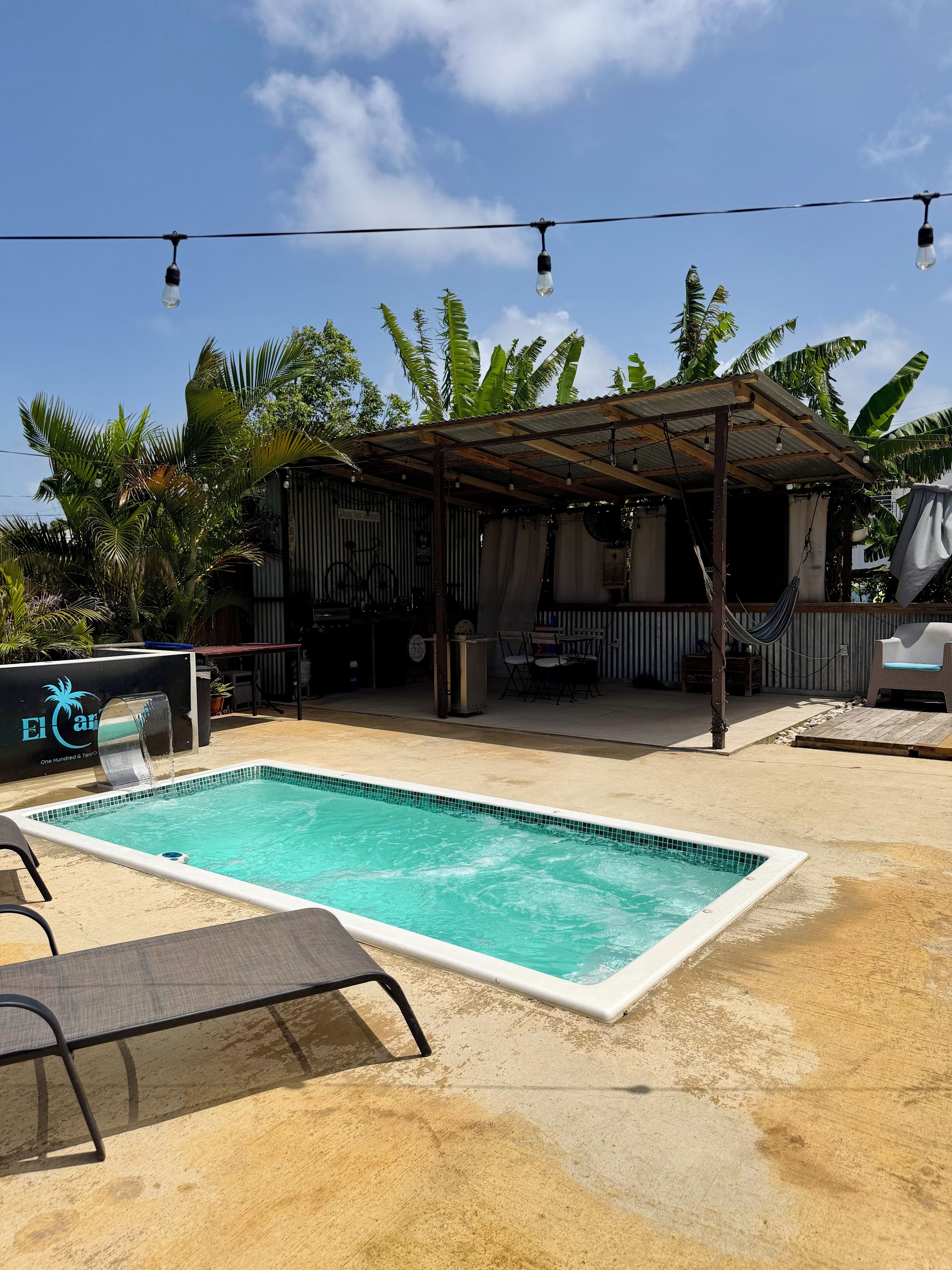 Ein Swimmingpool mit gefliestem Rand, umgeben von einer Sandfläche mit Liegestühlen.