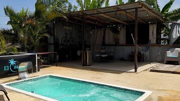 Ein Swimmingpool mit gefliestem Rand, umgeben von einer Sandfläche mit Liegestühlen.