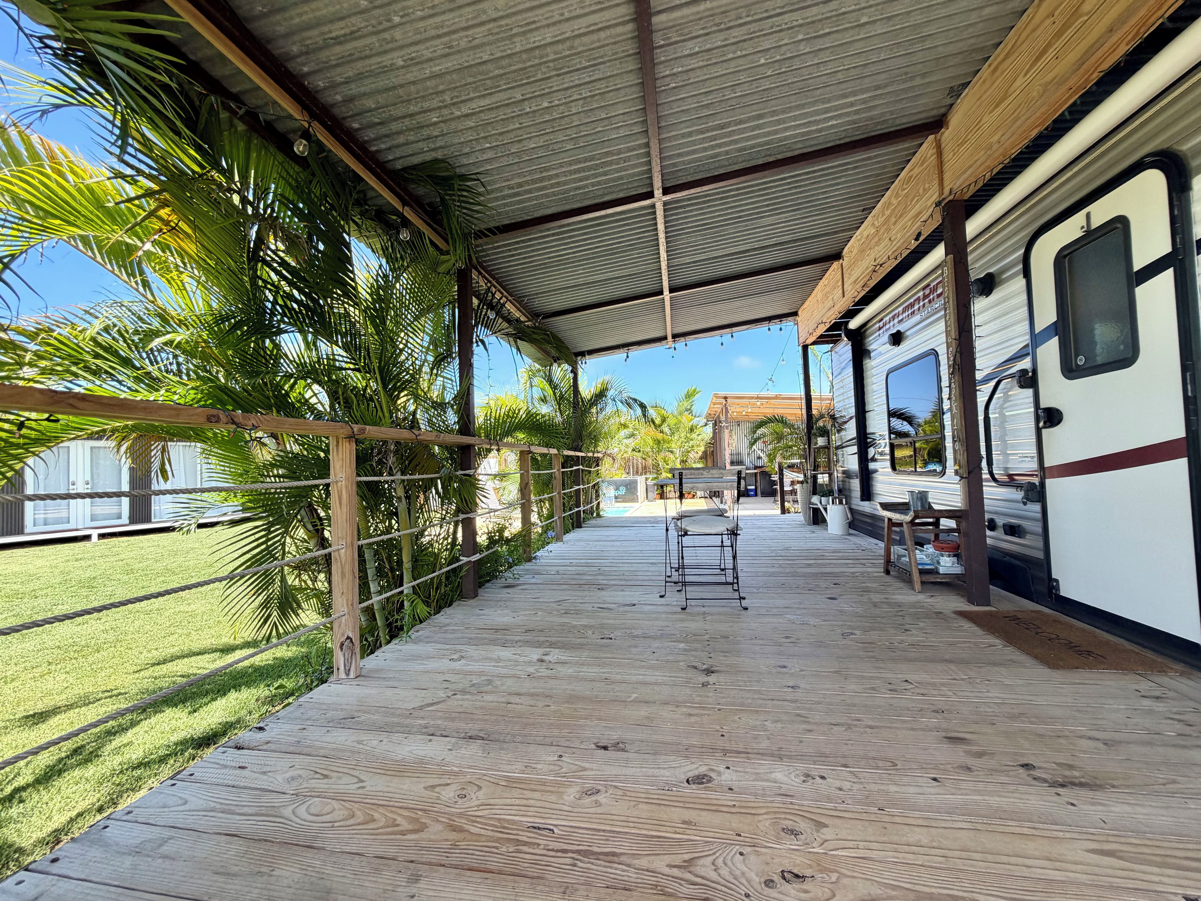 A covered deck with a wooden floor, a metal roof, and a white RV parked on the right.