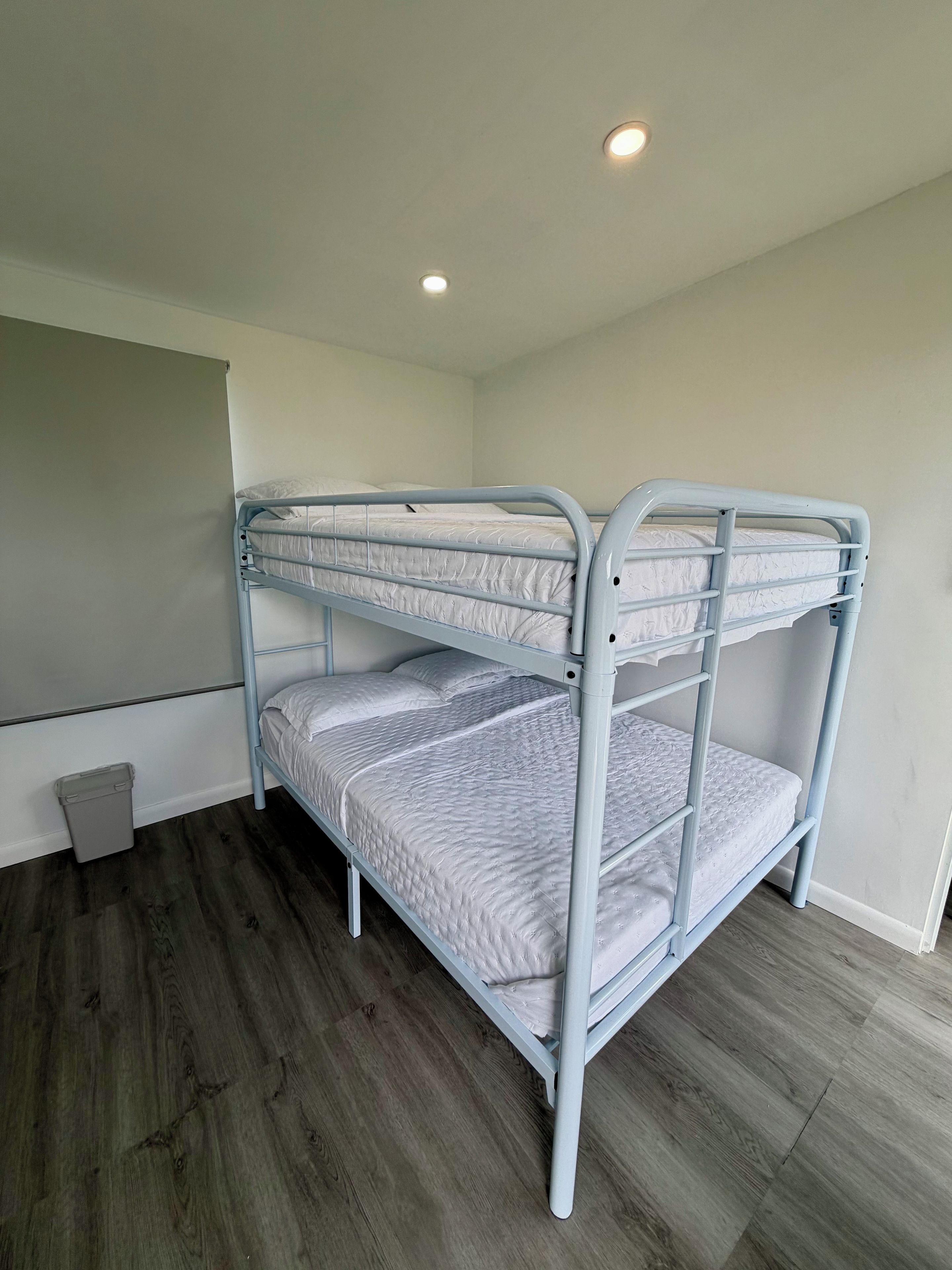 A bunk bed with a metal frame, a small trash bin, and a wooden floor.