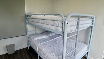 A bunk bed with a metal frame, a small trash bin, and a wooden floor.