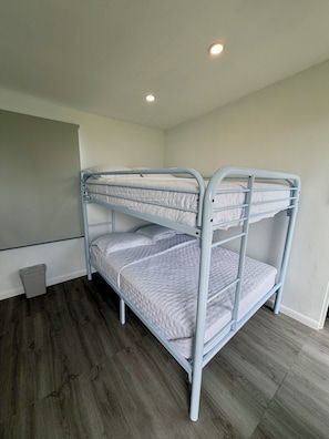 A bunk bed with a metal frame, a small trash bin, and a wooden floor. - EL Camper Retreat - Sleep 12  (Maleza Alta)