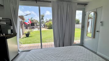 A bedroom with a large bed, sliding glass doors to a backyard, a small table with a coffee maker, and a mirror on the wall.