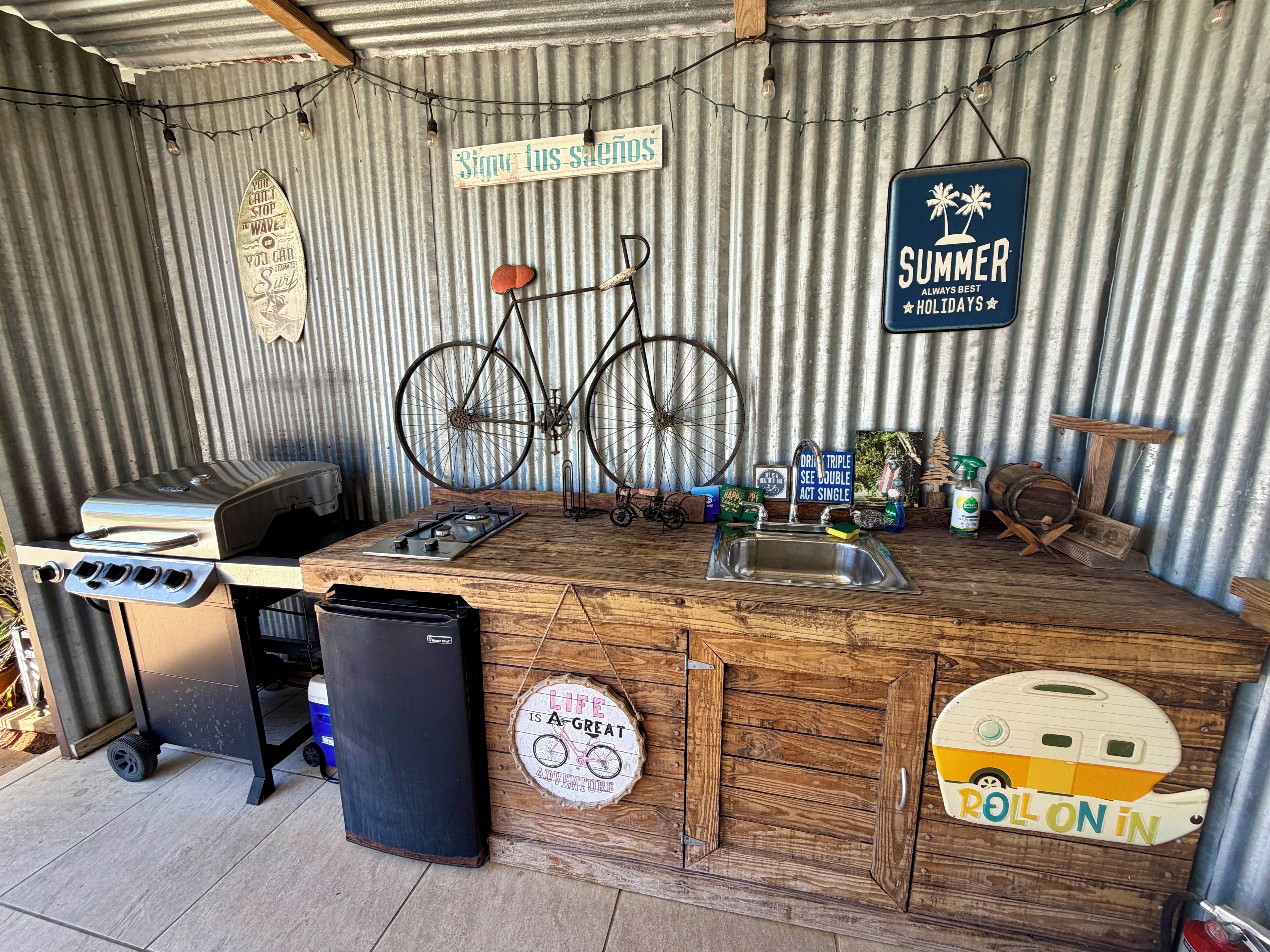 Una cocina rústica al aire libre con estufa a gas, lavamanos y una bicicleta.