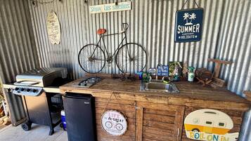 Una cocina rústica al aire libre con estufa a gas, lavamanos y una bicicleta.