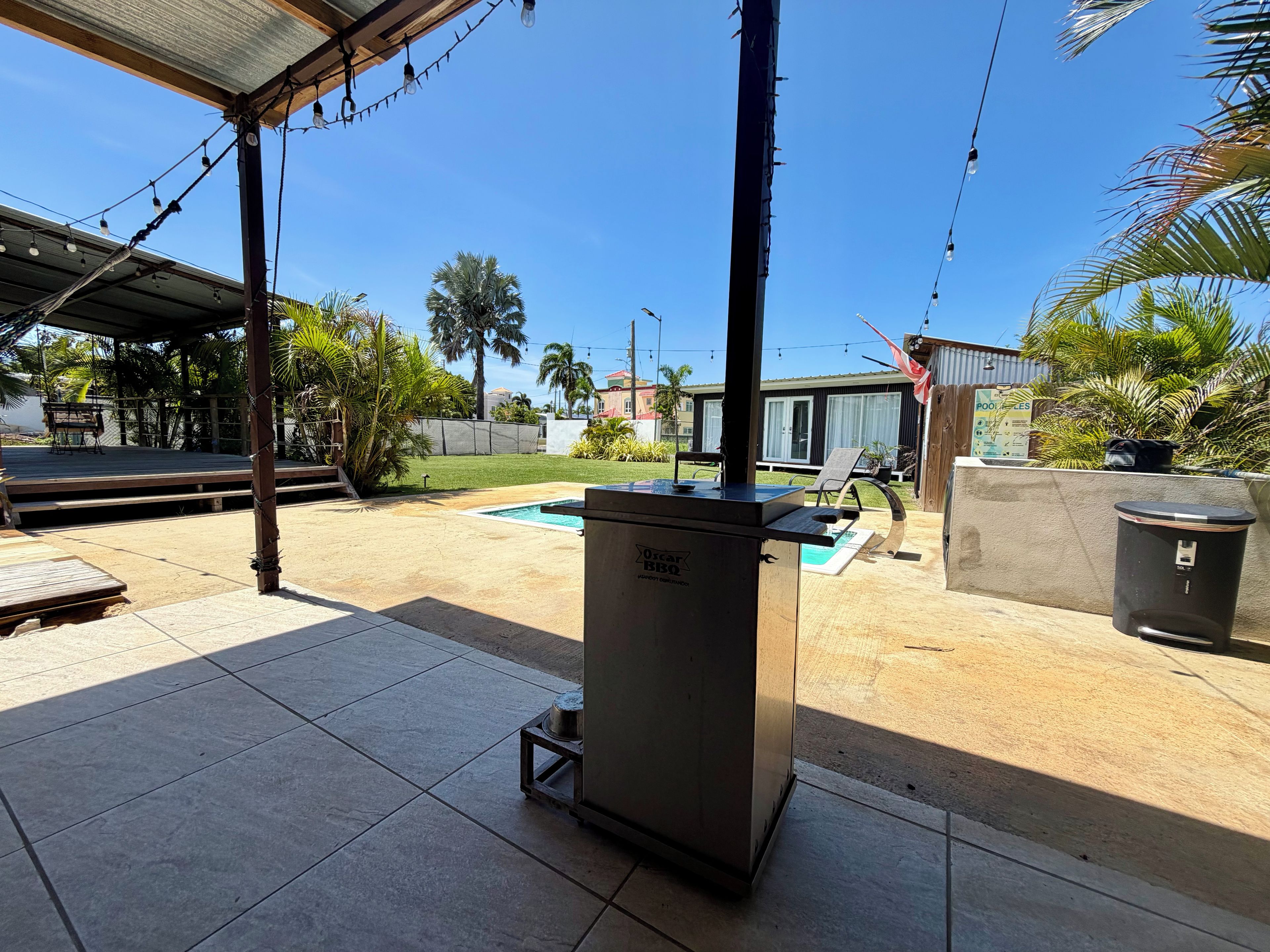 A covered outdoor area with a pool, a barbecue grill, and a trash can.