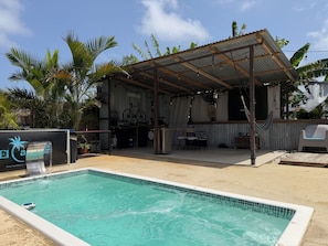 A pool area with a covered seating area, a grill, and a sign that reads 'El Ca.'