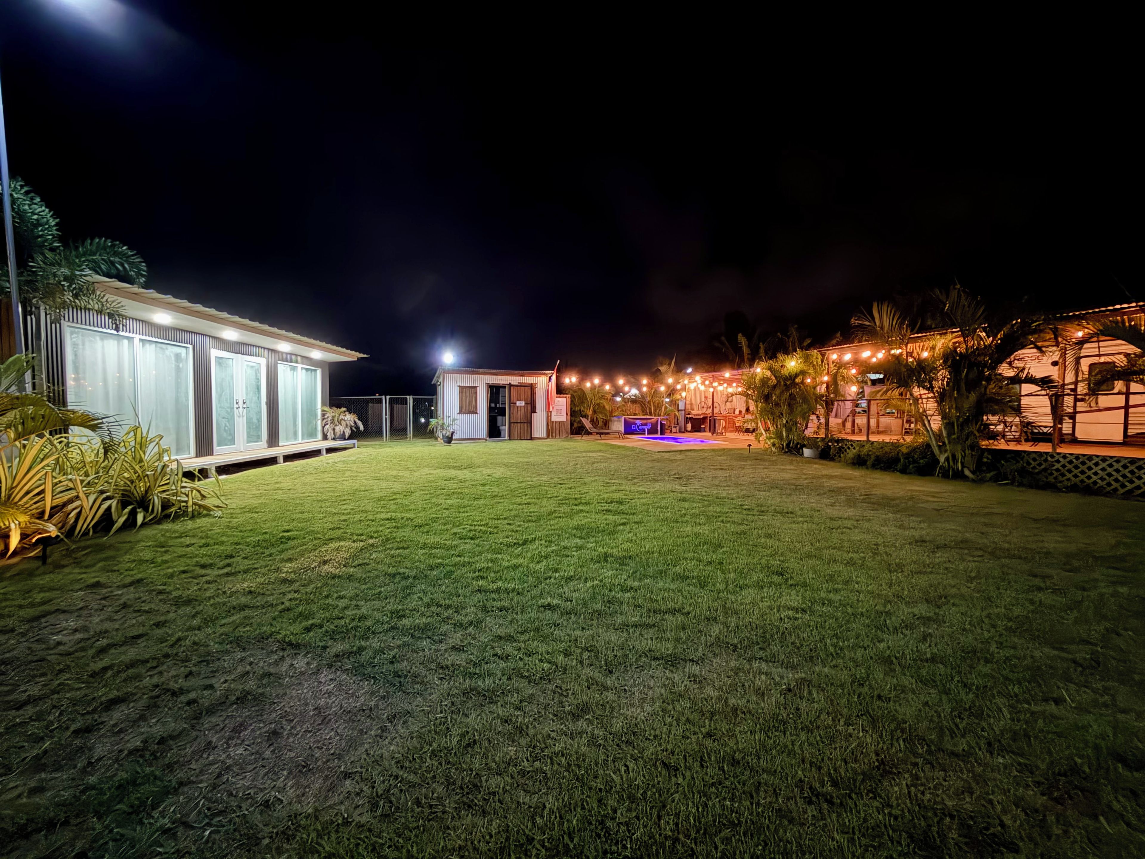 A well-lit outdoor area with a grassy lawn, a small building with a door, and string lights.
