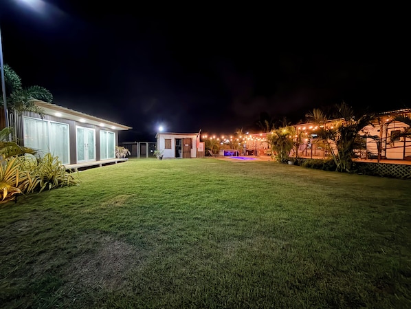 A well-lit outdoor area with a grassy lawn, a small building with a door, and string lights.