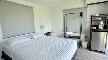 A hotel room with a large bed, a small kitchenette, and a window.