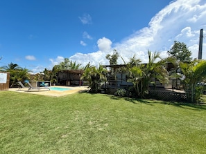 A backyard with a swimming pool, lounge chairs, and a covered patio area.