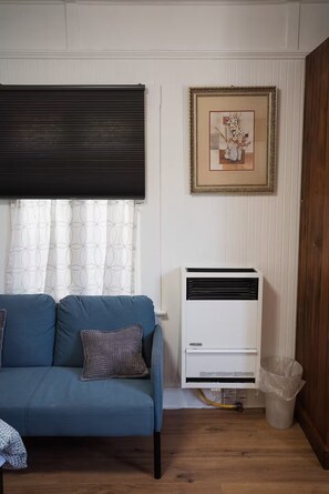 A room with a blue sofa, a framed picture on the wall, and an air conditioning unit. - 2336B - Lovely Backyard Studio near UC Berkeley (Berkeley)
