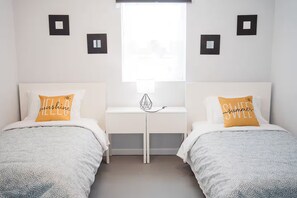 Una habitación con dos camas, una mesita de noche pequeña y una ventana.