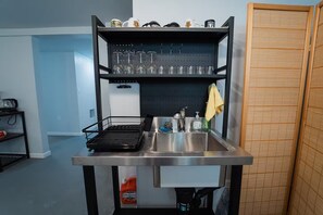 A compact kitchen with a stainless steel sink, a drying rack, and a pegboard above the sink holding various kitchen items. - 2336C - Ground 2B1B Unit with Laundry TV near UCB (Berkeley)
