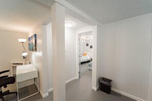A hallway leading to a bedroom with a bed, a desk with a lamp, and a trash bin. - 2336C - Ground 2B1B Unit with Laundry TV near UCB (Berkeley)