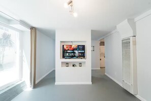 A modern hallway with a mounted television displaying a Disney+ interface, a white wall, and a window with curtains. - 2336C - Ground 2B1B Unit with Laundry TV near UCB (Berkeley)