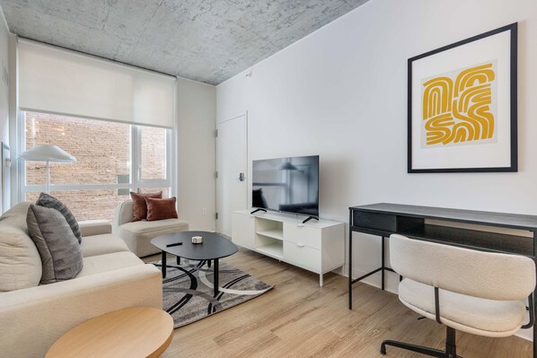 Uma sala de estar moderna com sofá, mesa de centro, televisão e escrivaninha com cadeira.