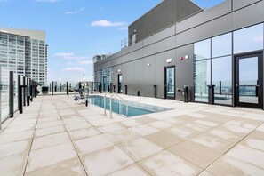 Uma área de piscina no terraço com vista desimpedida para o horizonte da cidade, um edifício moderno com grandes janelas e uma piscina com guarda-corpos de segurança.
